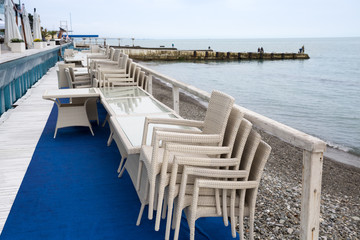 Row of wicker chairs stacked on each other and cafe tables along the embankment. Start/end of tourist season