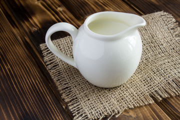 Milk in the ceramic jug on the wooden background