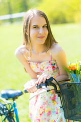 Portrait of young beautiful woman with long hair in summer park. Beside a bicycle with a basket of flowers