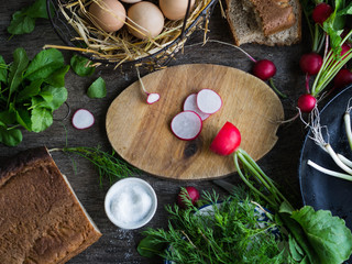 Ingredients for breakfast - fresh eggs in a wire basket, fresh herbs - spinach, dill and green onions, fresh radish with tops, salt, rye bread. Rustic style. Top view