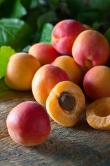 Juicy fresh apricots with leaves on old wooden table .