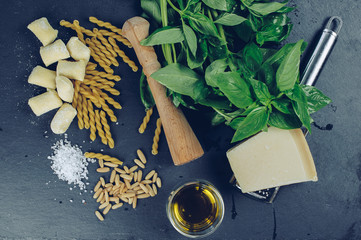Raw ingredients for pesto sauce: basil pine nuts, parmesan, olive oil with uncooked pasta and...