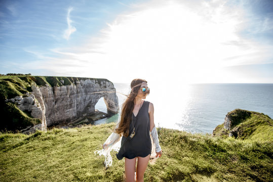 Young woman dressed in hippie style enjoying nature on the rocky coastline with great view on the ocean in France