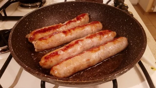 Appetizing ruddy juicy sausages fried in oil in a large frying pan