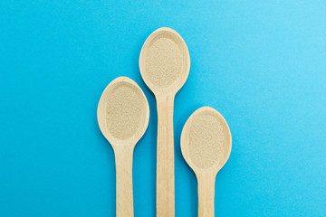 Three wooden spoons with instant dry yeast isolated on a blue background. Yeast is the main ingredient of fresh dough for pastry, pizza dough and many other dough.