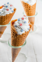 Treats for Independence Day holiday on July 4. Homemade cream ice cream in waffles, decorated with stars in traditional colors - blue, red, white. On a white wooden table, copy space