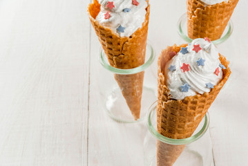 Treats for Independence Day holiday on July 4. Homemade cream ice cream in waffles, decorated with stars in traditional colors - blue, red, white. On a white wooden table, copy space