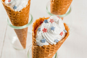 Treats for Independence Day holiday on July 4. Homemade cream ice cream in waffles, decorated with stars in traditional colors - blue, red, white. On a white wooden table, copy space