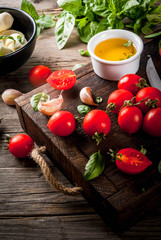 Farm raw organic products. Preparation of dinner in the Italian style. Ingredients for caprese salad, pasta, pizza. Basil, tomatoes, mozzarella cheese, olive oil on an old wooden table.