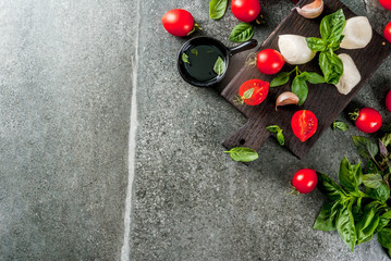 Farm raw organic products. Cooking of dinner in Italian style. Ingredients for caprese salad, pasta, pizza. Basil, tomatoes, mozzarella cheese, olive oil. dark grey stone table. Copy space top view