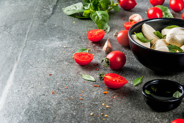 Farm raw organic products. Cooking of dinner in Italian style. Ingredients for caprese salad, pasta, pizza. Basil, tomatoes, mozzarella cheese, olive oil. dark grey stone table. Copy space