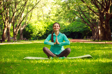 Young woman in summer park doing yoga with closed eyes