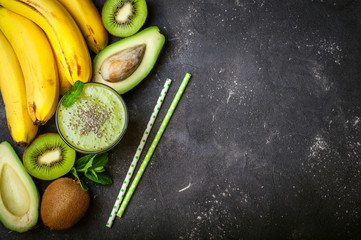 Healthy green smoothie and ingredients on dark background. Kiwi smoothie with fruits. Concept superfoods, diet, detox, health, vegetarian food. Top view