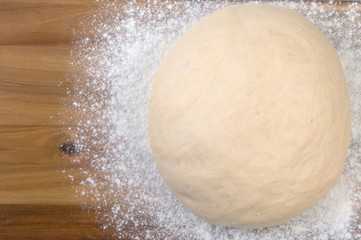Ball a dough and white flour on a wooden cutting board. Top view, close up.