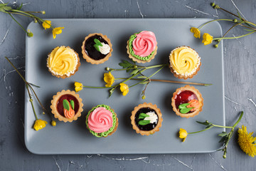 Row of Colorful cupcakes on grey plate and table. Cakes with cream and jam. Yellow flowers on a background