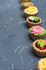 Row of colorful cupcakes on grey table. Cakes with cream and jam on a stone background