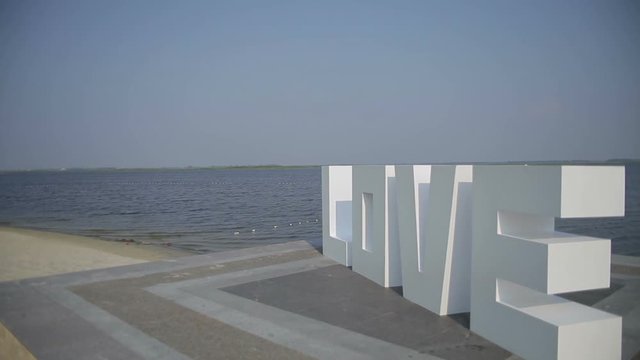 White letters forming word LOVE standing near river, LOVE letters, wedding decorations, valentines day. Steadicam shot.