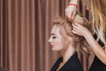 Hairdresser makes evening hairstyle close-up on blond hair of business woman in beauty salon