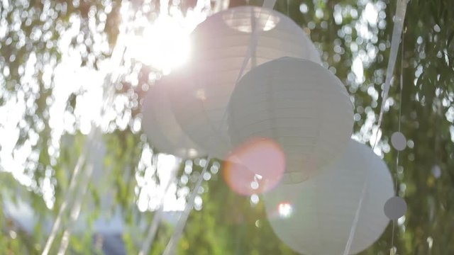 White chinese lantern hanging on a tree. White lanterns blow gently in the breeze at sunrise  gently swaying in the wind. Valentine Day. Wedding day.