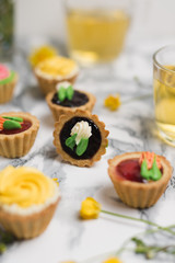Colorful cupcakes on grey marble table. Cakes with cream and jam. Cup of green tea and yellow flowers on a background