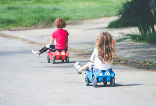 Children Playing On The Street Driving Toy Cars