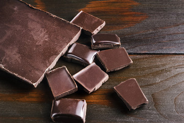 Bitter, dark chocolate bar and broken cubes on wooden background