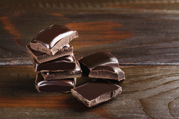 Pieces of bitter, dark chocolate, cubes on heap at wooden background, close-up view