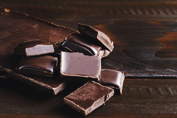 Pieces of bitter, dark chocolate, cubes on heap at wooden background, close-up view