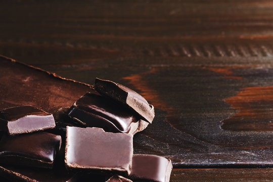 Pieces of bitter, dark chocolate, cubes on heap at wooden background, close-up view