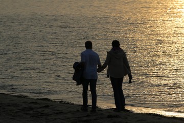 Paar schlendert h&auml;ndchenhaltend am Strand bei romantischem Sonnenuntergang