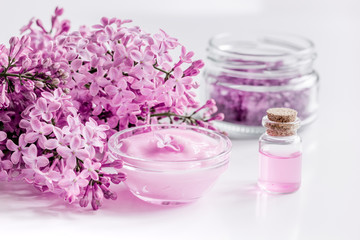 Fototapeta na wymiar spa cosmetic set with lilac flowers white desk background