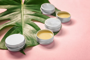 Jars with balsam and green tropical leaf on color background, closeup. Natural cosmetics concept
