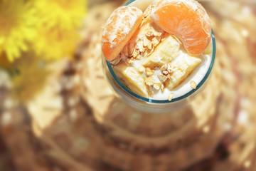 Yoghurt with muesli and fresh fruit, banana and tangerine in a glass bowl next to yellow flowers