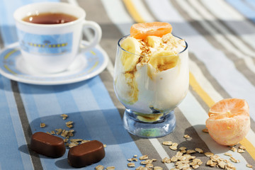 Yoghurt with muesli and fresh fruits and tangerine and a cup of tea for a call