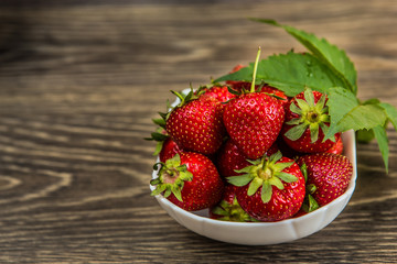 Small white china bowl filled with succulent juicy fresh ripe red strawberries on an old wooden textured table top. Fresh strawberries. strawberries on a wooden table