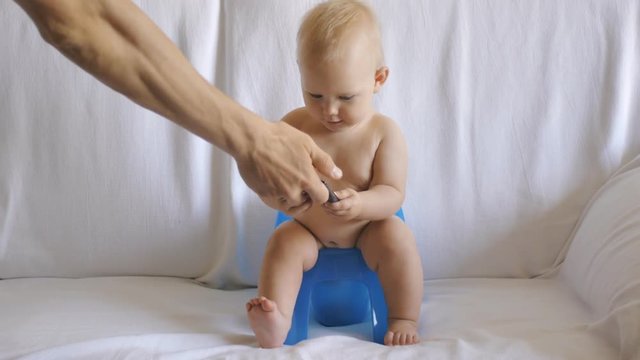 Baby sits on potty using smartphone. Male hand gives phone to cute ten months old baby sitting on blue potty.