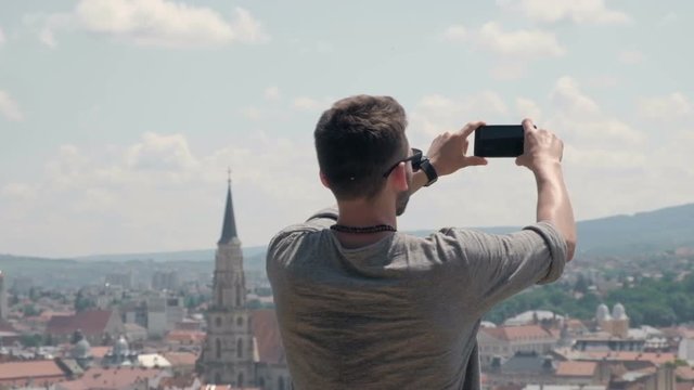 Male traveller make a panoramic photo of the old city to his phone for Instagram or other social networks. Travel to Romania.