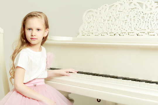 A little girl is sitting at the white piano.