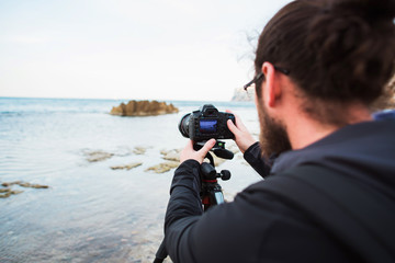 Young photographer making photos of sea with the camera on a tripod