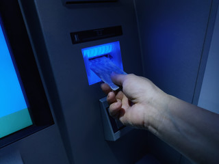 Hand inserting ATM card into bank machine to withdraw money