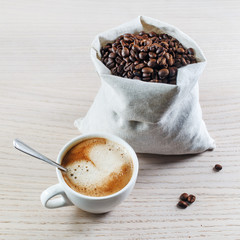 Photo of coffee cup and coffee beans in a canvas bag on wooden table background.