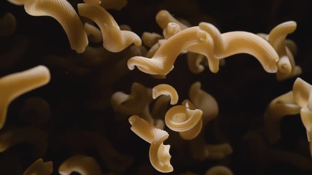 Raw cellentani pasta flies after being exploded against black background. Shot with high speed camera, phantom flex 4K. Slow Motion.