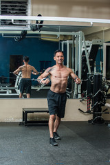 Fototapeta na wymiar Middle age muscular man performing cable chest press exercise with back reflected in mirror and intense expression. 