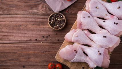Chicken drumstick on a wooden brown board standing on a wooden background, a jar of peppers, a brown napkin. The process of cooking. Healthy food