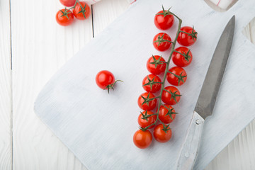 Branches of cherry tomatoes with knife on a white wooden board standing on white wooden background