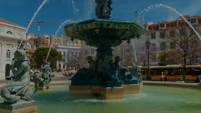 Establishing shot of Lisbon, Portugal - A revolving shot around a water fountain in the Rossio Square - Praca do Rossio. 