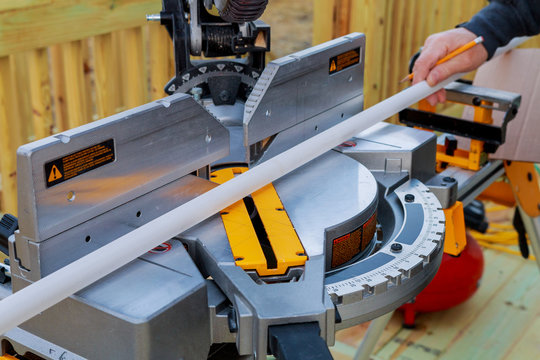 Closeup of mature man sawing lumber with sliding compound miter saw outdoors, sawdust flying around