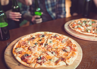 Friends having a drinks in a bar, They are sitting at a wooden table with beers and pizza.