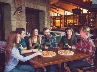 Friends having a drinks in a bar, They are sitting at a wooden table with beers and pizza.