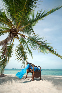 wicker chair in the shade of palm tree on beach